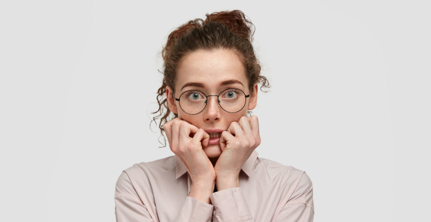 unhappy-nervous-young-female-with-worried-expression-bites-finger-nails-looks-anxiously-directly-wears-spectacles-dressed-fashionable-clothes-stands-against-white-wall unhappy-nervous-young-female-with-worried-expression-bites-finger-nails-looks-anxiously-directly-wears-spectacles-dressed-fashionable-clothes-stands-against-white-wall