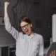 business-woman-with-laptop-hand-is-happy-with-success-portrait-woman-glasses-striped-blouse-enthusiastically-screaming-making-winning-gesture