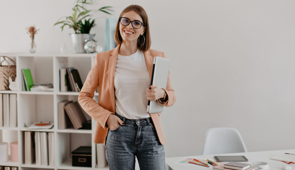 satisfied-female-entrepreneur-posing-with-laptop-hand-against-her-minimalistic-office