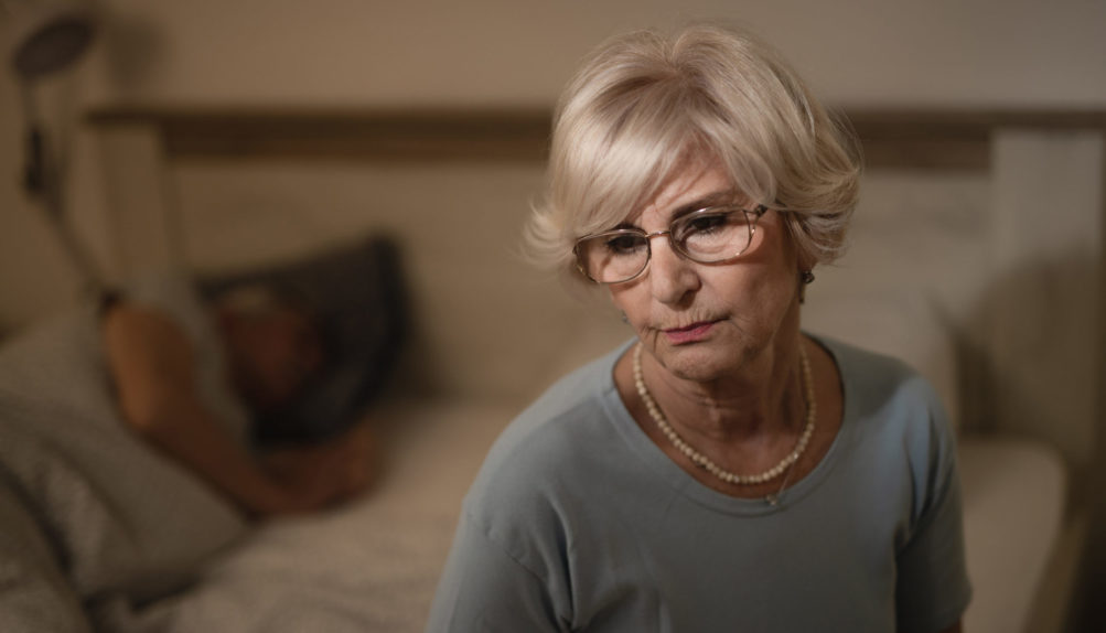 thoughtful-mature-woman-sitting-bedroom-evening-while-her-husband-is-sleeping-background