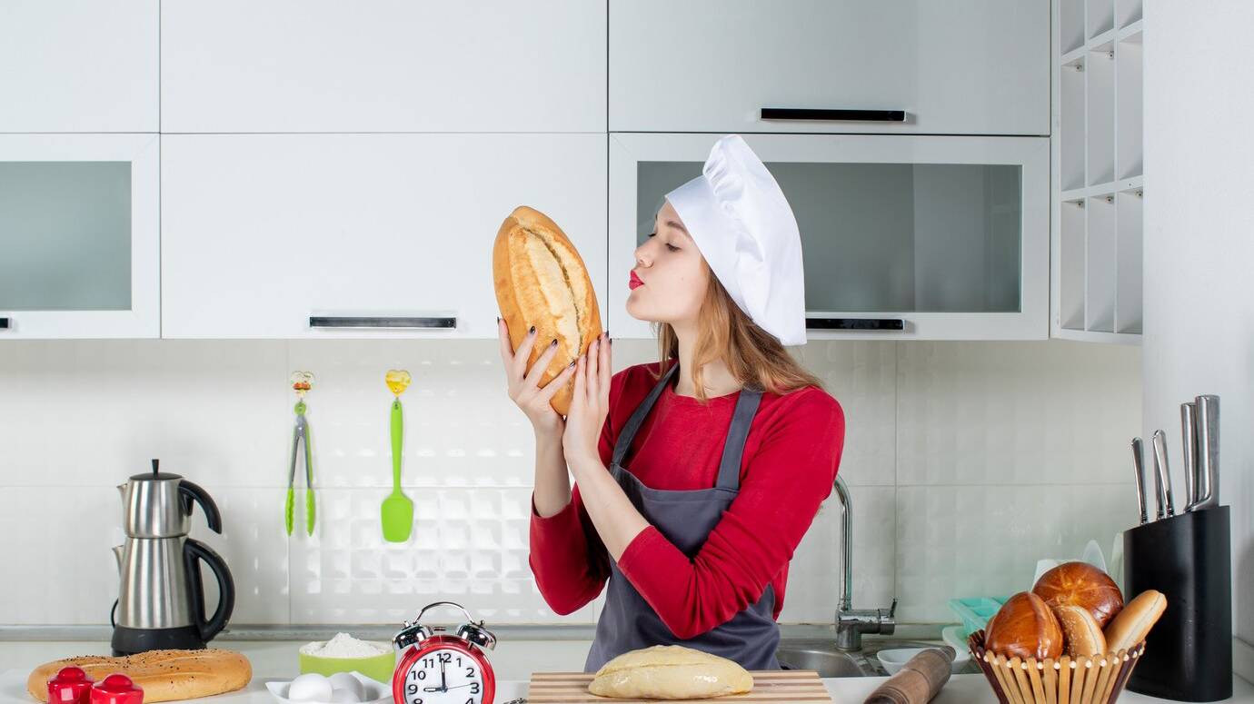 front-view-pretty-woman-in-cook-hat-and-apron-smelling-bread-in-the-kitchen_140725-109430