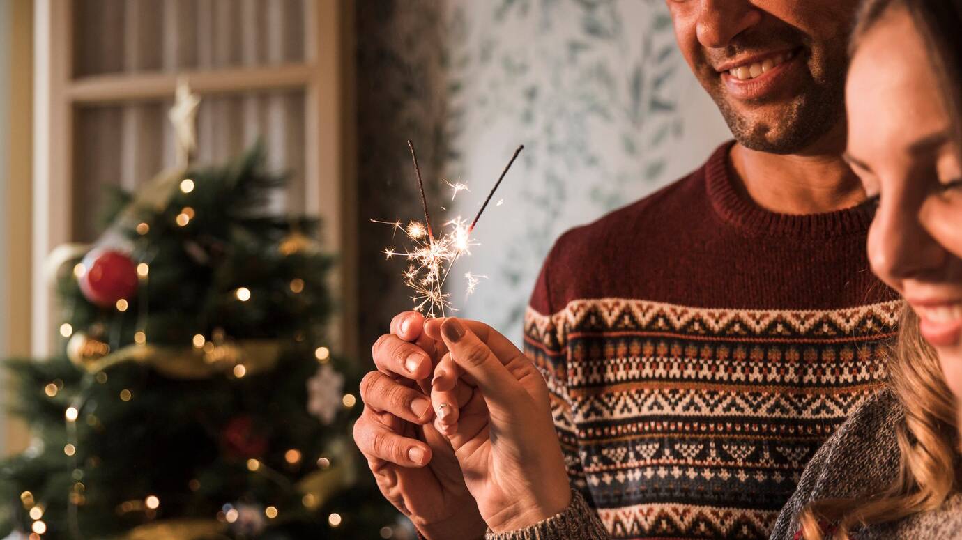 smiling-guy-and-cheerful-woman-with-flaming-bengal-lights-near-christmas-tree_23-2147987556