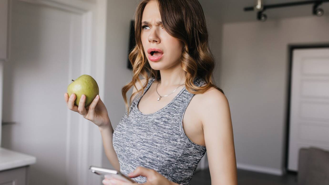 dark-haired-girl-with-nude-makeup-posing-home-with-smartphone-unhappy-young-woman-with-apple-phone-standing-with-mouth-open_197531-9738