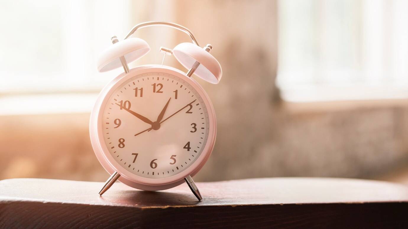 pink-alarm-clock-wooden-table-sunlight_23-2147943472