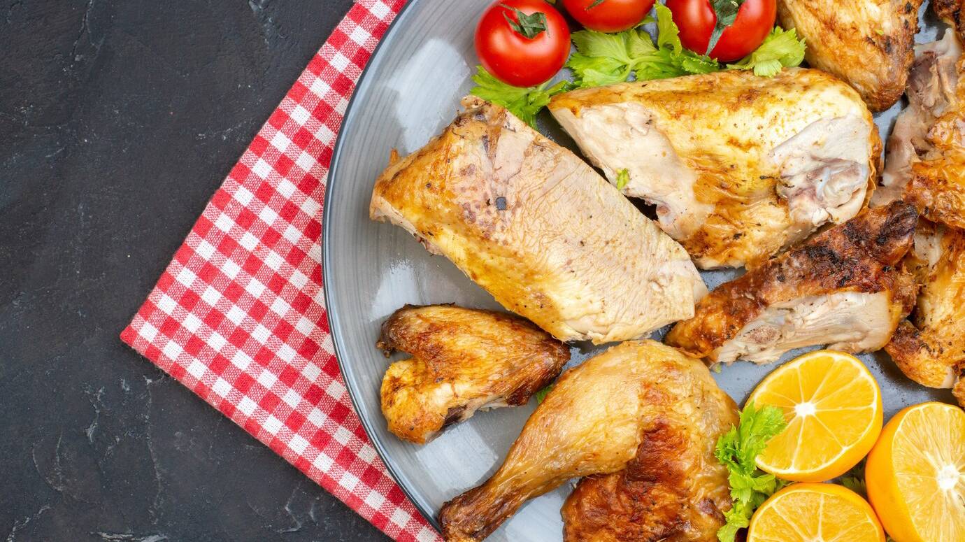 top-half-view-baked-chicken-fresh-tomatoes-lemon-slices-plate-napkin-black-table_140725-148762