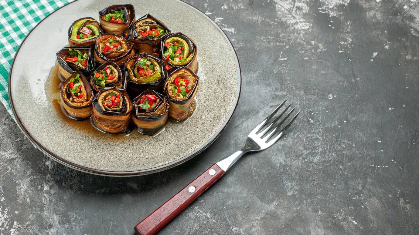 front-view-stuffed-aubergine-rolls-white-oval-plate-turquoise-white-tablecloth-fork-grey-free-place_140725-105818