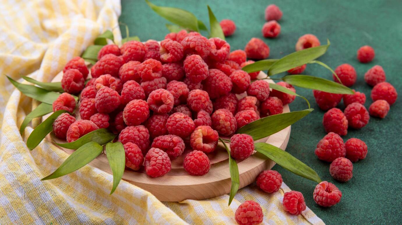 side-view-raspberries-with-leaves-cutting-board-plaid-cloth-green_141793-16718