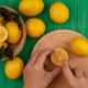 top-view-female-hands-cutting-lemon-wooden-kitchen-board-with-knife-with-lemons-bucket-green-wooden-wall_141793-76020