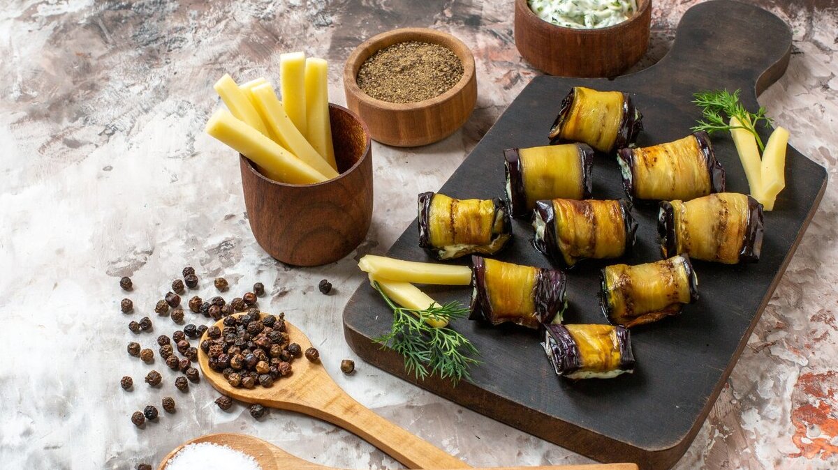 bottom-view-grilled-eggplant-rolls-wood-cutting-board-spices-wooden-spoons-nude-background_140725-106348