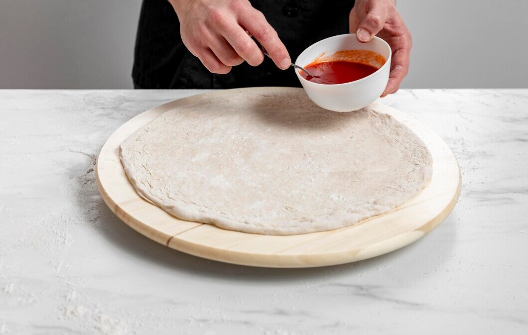 high-angle-man-spreading-tomato-sauce-pizza-dough_23-2148785719