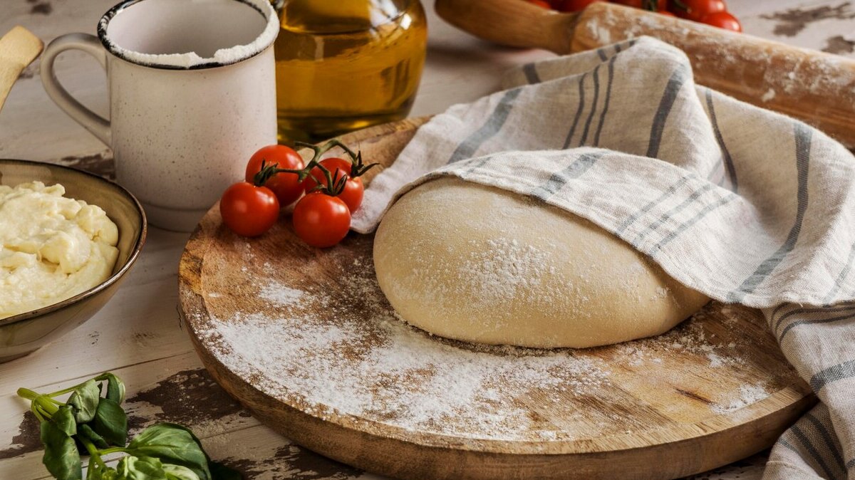 pizza-dough-covered-with-cloth-oil-tomatoes_23-2148753769