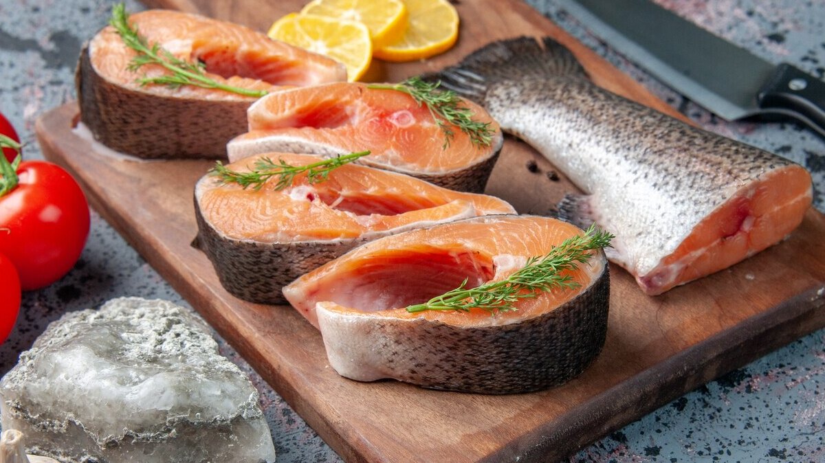 side-view-raw-fishes-lemon-slices-greens-pepper-wooden-cutting-board-vegetables-knife-blue-black-colors-table_179666-18204