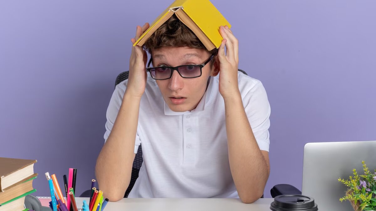 student-guy-white-polo-shirt-wearing-glasses-sitting-table-holding-book-his-head-looking-confused-blue-surface_141793-108898