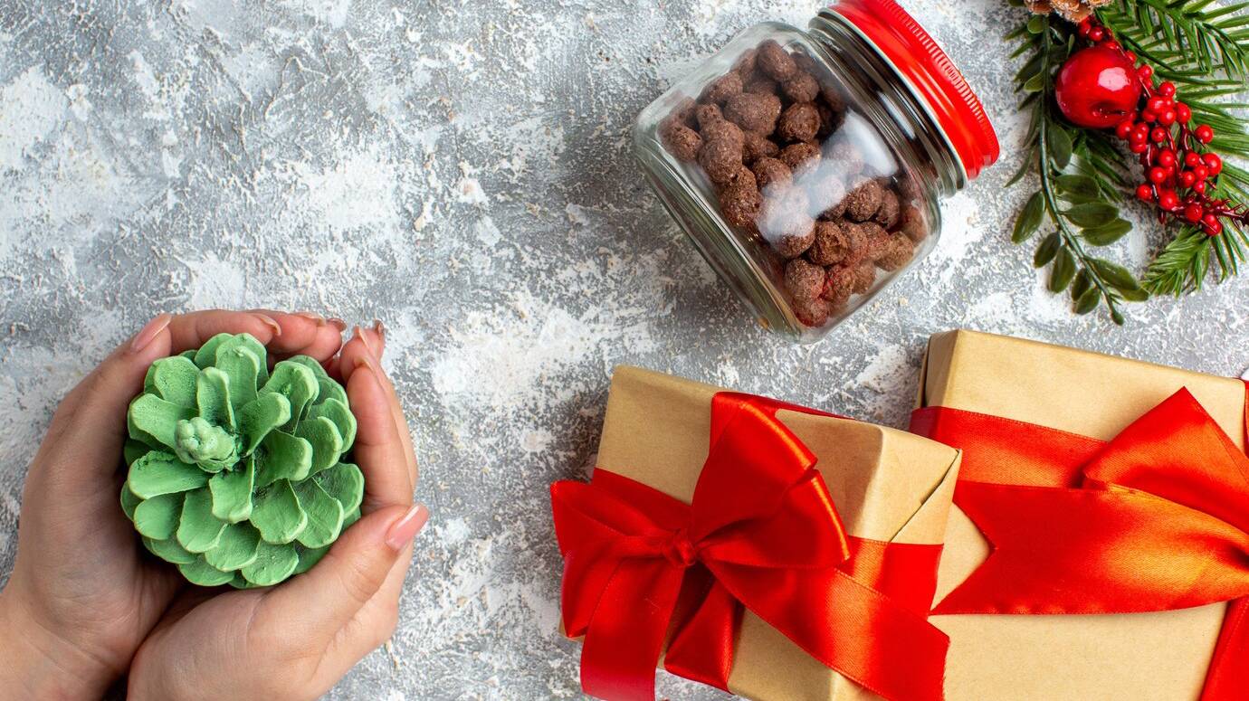 top-view-xmas-gifts-cereal-jar-green-cone-female-hand-grey-table_140725-132375