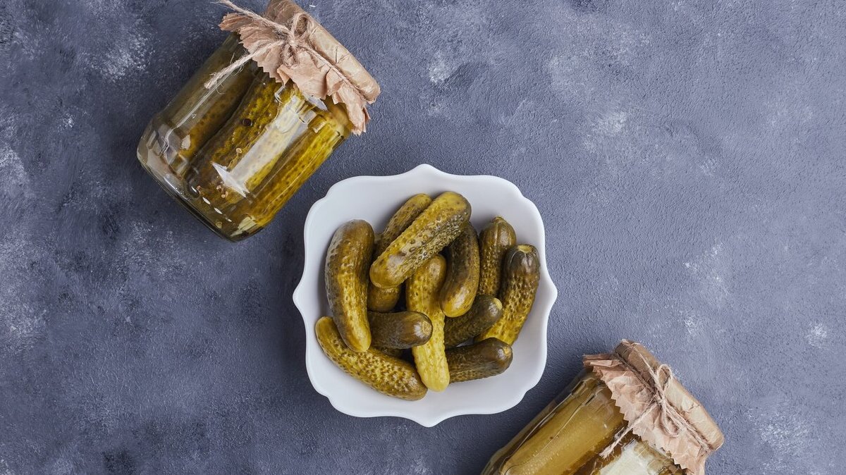 pickled-cucumbers-bowl-glass-jars-blue-background_114579-14710