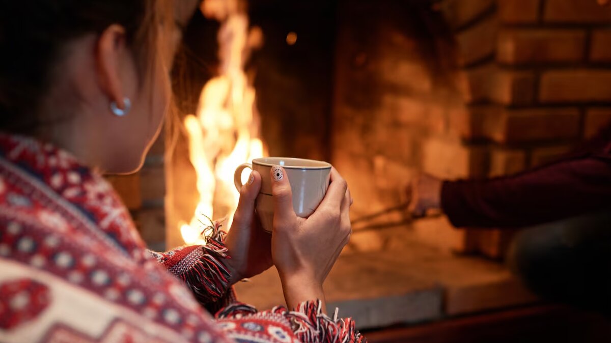 shoulder-shot-woman-warming-her-hands-mug-hot-tea-sitting-fireplace-her-boyfriend-dealing-with-charcoal_1098-19374